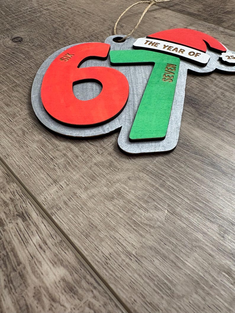 May include: Wooden Christmas ornament with the numbers 6 and 7 in red and green, with the words "SIX" and "SEVEN" on the numbers. The ornament also features a Santa hat and the words "THE YEAR OF".