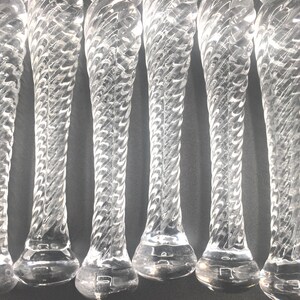May include: A close-up of several clear glass stems with a twisted design. Each stem has a bulbous base and a rounded top. The glass has a reflective quality, and the stems are arranged in a row.