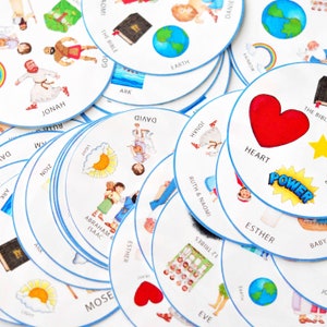 May include: A set of colorful, round, paper game pieces with images and text related to the Bible. The pieces feature images of a heart, a rainbow, a globe, an ark, a book, a sun, a person with a staff, and a group of people. The text on the pieces includes words like "Jonah", "David", "Esther", "Power", "Heart", "Earth", "The Bible", "Ark", "Light", "12 Tribes", "Ruth & Naomi", "Abraham & Isaac", "Eve", "Moses", and "Jonah".