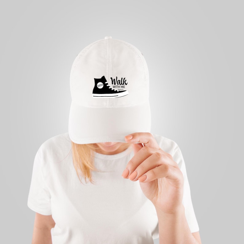 May include: White baseball cap with a black graphic of a high-top sneaker and the words "Walk With Me". The sneaker design includes the year "2024". The cap has a curved brim and a fabric strap closure.