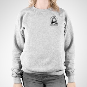 May include: A light gray sweatshirt with a crew neck. The sweatshirt features a small black graphic of Jesus with a halo and the text "WALK WITH ME + 2024" printed below the graphic. The sweatshirt is made of a soft material.