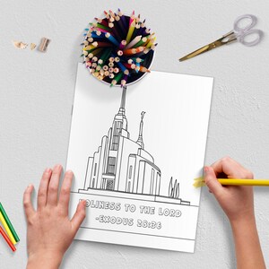 May include: A coloring page featuring a detailed line drawing of a temple with the text "HOLINESS TO THE LORD - EXODUS 28:36". A child is coloring the page with a yellow pencil. Colored pencils, scissors, and pencil shavings are scattered around.