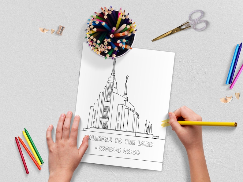 May include: A coloring page featuring a detailed line drawing of a temple with the text "HOLINESS TO THE LORD - EXODUS 28:36". A child is coloring the page with a yellow pencil. Colored pencils, scissors, and pencil shavings are scattered around.