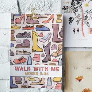 K&ouml;nnte beinhalten: Ein Druck mit bunten Schuhillustrationen, darunter Stiefel, Abs&auml;tze und Turnschuhe, vor einem hellrosa Hintergrund. Der Text "WALK WITH ME MOSES 6:34" ist unten zu sehen. Der Druck wird von einer goldenen Klammer gehalten.