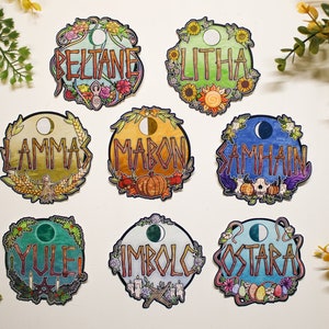 May include: Eight colorful round stickers with illustrations and text depicting the eight major holidays in the Wheel of the Year. The stickers feature the names of the holidays: Yule, Imbolc, Ostara, Beltane, Litha, Lammas, Mabon, and Samhain.