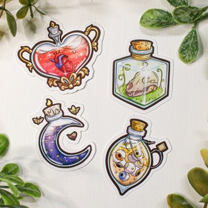 Puede incluir: Cuatro botellas de vidrio con diferentes contenidos y tapones de corcho. Las botellas tienen forma de corazón, cubo, media luna y lágrima. La botella en forma de corazón contiene un líquido rojo con un corazón en su interior. La botella en forma de cubo contiene una calavera y follaje verde. La botella en forma de media luna contiene un líquido azul con estrellas y mariposas. La botella en forma de lágrima contiene un líquido amarillo con ojos.