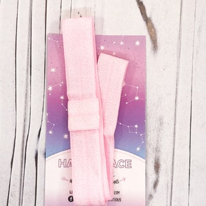 May include: A light pink hair tie with a matching card featuring a constellation design and the text "HAIR ACE". The hair tie is made of a soft, stretchy material. The card has a gradient of pink and purple.