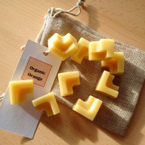 May include: A burlap pouch filled with small, square-shaped, orange-colored wax melts. The pouch has a tag attached that reads "Organic Orange".