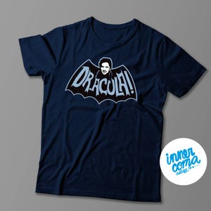 May include: A navy blue t-shirt with a graphic of a person in a bat costume with the text "DRACULA!" in white letters.