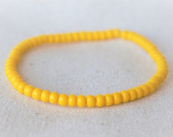May include: A bright yellow beaded bracelet. The bracelet is made of small, round beads strung together to form a flexible band. The beads are a solid, sunny yellow color, and the bracelet is displayed on a white surface.