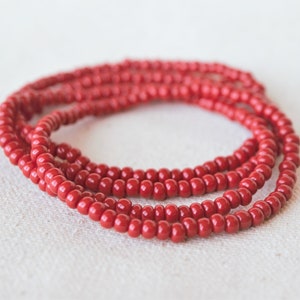May include: A red beaded bracelet with multiple strands. The bracelet is made of small, round beads that are strung together to create a simple and elegant design.