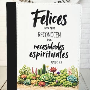 Puede incluir: Una cubierta de Biblia blanca con el texto en español "Felices los que reconocen sus necesidades espirituales" y "Mateo 5:3". La cubierta presenta un lomo negro y un diseño colorido de suculentas y cactus en la parte inferior.