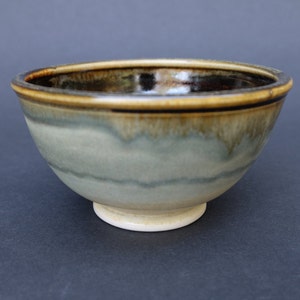 May include: A small, ceramic bowl with a light blue glaze and brown rim. The bowl has a slightly raised base.