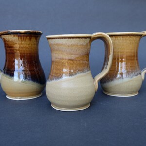 May include: Three ceramic mugs with brown and beige glaze. The mugs have a rounded body and a handle.