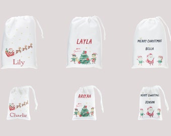 May include: Six white Christmas gift bags with different designs. The bags feature Santa Claus, elves, reindeer, and a Christmas tree. The bags are personalized with names like Lily, Layla, Bella, Charlie, Ariyah, and Jenson.
