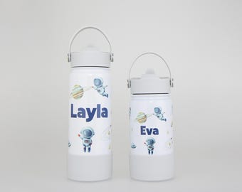 May include: Two white stainless steel water bottles with light gray lids and silicone bases. Each bottle features a watercolor space theme with astronauts and planets. The taller bottle is personalized with the name Layla, and the shorter bottle is personalized with the name Eva in dark blue lettering.