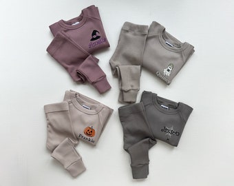 May include: A collection of children's Halloween-themed pajamas in various muted colors. Each set includes a long-sleeved top and matching pants. Tops are embroidered with a witch hat, ghost, pumpkin, and spiderweb, each with a name.