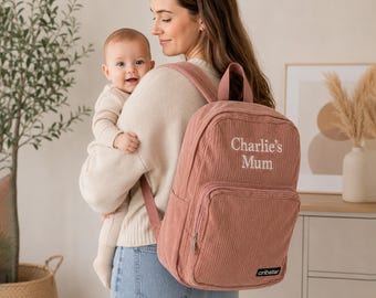 May include: A dusty rose corduroy backpack with the text "Charlie's Mum" embroidered in white. The backpack has a front pocket and adjustable straps. The brand name "cribstar" is at the bottom. The backpack is being worn.