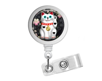 May include: White lucky cat with a red collar and gold coin charm, with a black and white background of flowers and geometric patterns, on a white retractable badge holder.