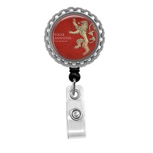 May include: A silver-toned retractable badge holder with a red and gold round button featuring a lion and the text "House Lannister Hear Me Roar".