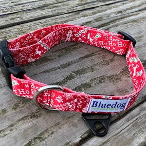 Può includere: Collare per cani rosso e bianco con un motivo natalizio con renne, fiocchi di neve e le parole "Ho Ho Ho". Il collare ha una fibbia nera e un anello a D argentato. Il collare ha anche un'etichetta nera che dice "Bluedog Pet Designs".
