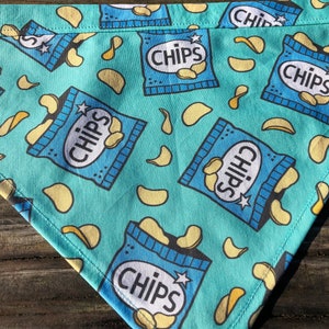 May include: A turquoise blue bandana with a repeating pattern of blue bags of chips with the word "CHIPS" printed on them and yellow potato chips scattered across the bandana.