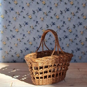 Op de afbeelding: Een kleine, bruine rieten mand met een geweven handvat. De mand staat op een licht houten oppervlak.