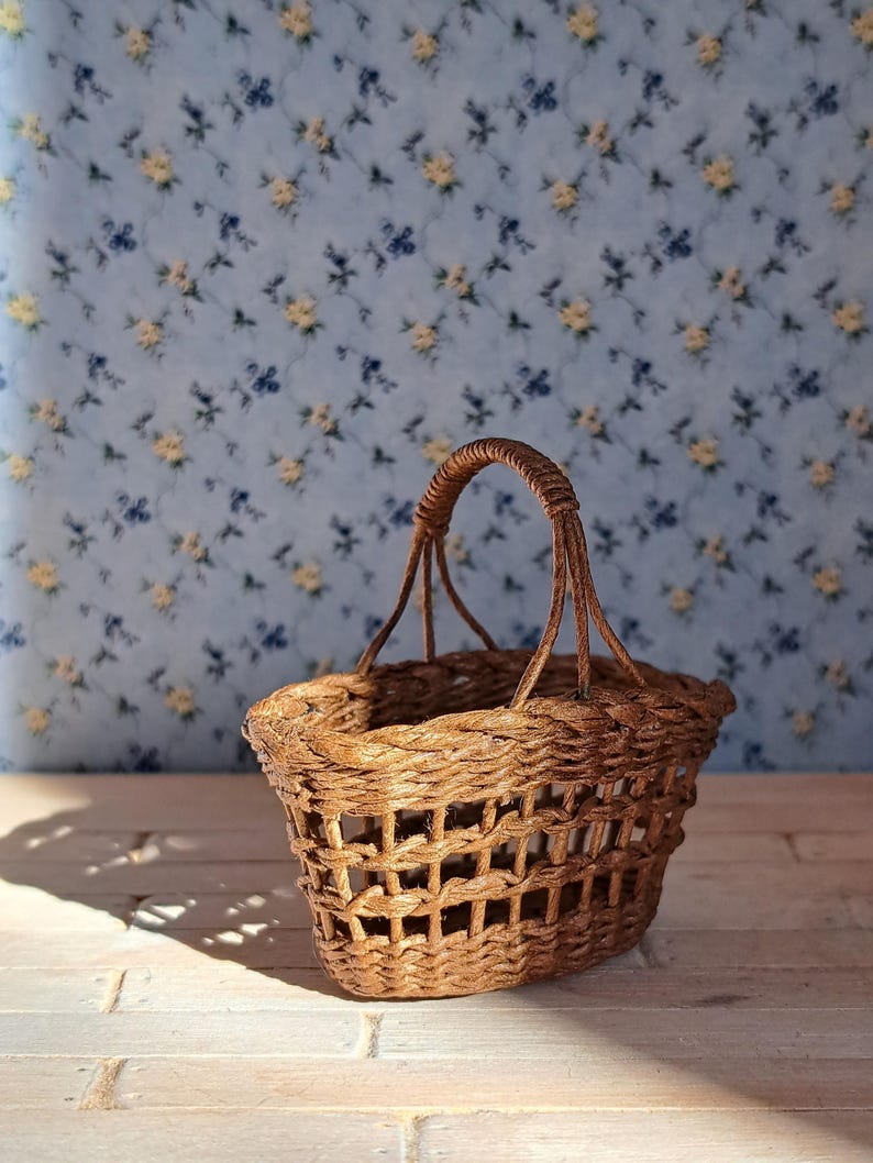 Op de afbeelding: Een kleine, bruine rieten mand met een geweven handvat. De mand staat op een licht houten oppervlak.