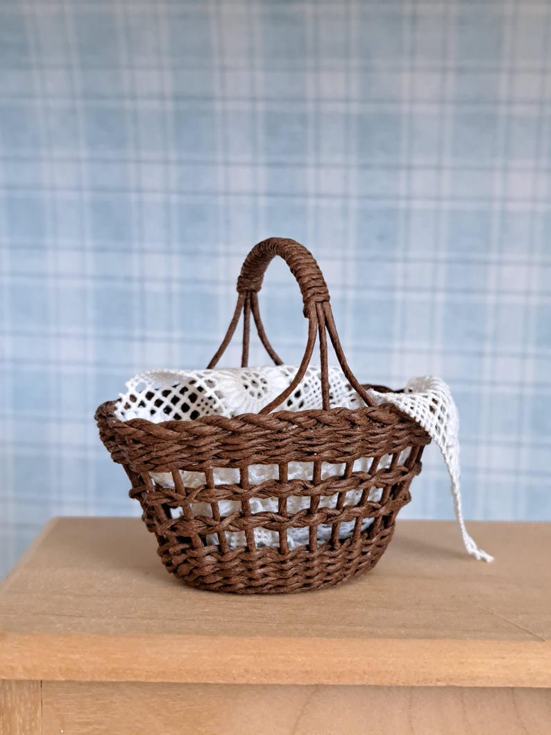 Op de afbeelding: Een bruine rieten mand met een wit kantje erin. De mand heeft een geweven handvat en staat op een houten oppervlak.