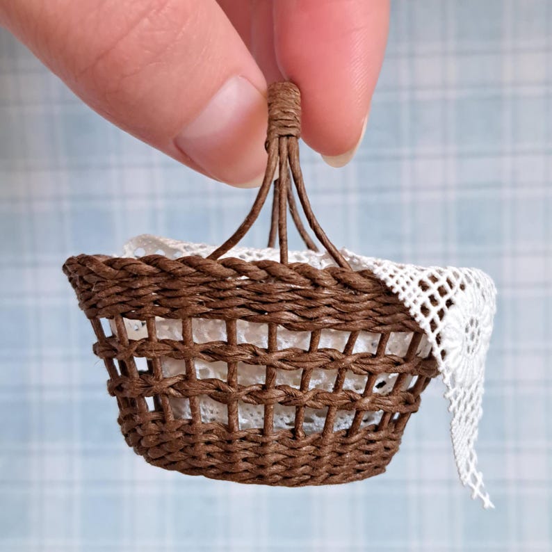 Op de afbeelding: Een klein bruin rieten mandje met een handvat en een witte gehaakte doily erin.