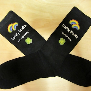 May include: A pair of black socks with a rainbow and shamrock design. The socks have the text "Lucky Socks - Transfer Day -" printed on them.