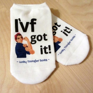 Może przedstawiać: Białe skarpetki do kostki z napisem "IVF got it!" i ilustracją kobiety zginającej ramię. Skarpetki mają również napis "Lucky Transfer Socks".