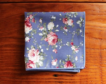 May include: A blue pocket square with a floral pattern featuring pink and white roses. The fabric has a subtle sheen and a light blue border.