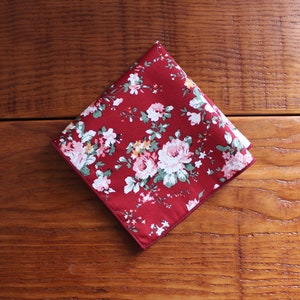 May include: A red cotton handkerchief with a floral pattern. The handkerchief has a white border.