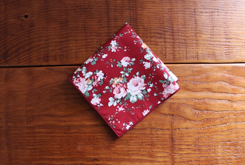 May include: A red cotton handkerchief with a floral pattern. The handkerchief has a white border.