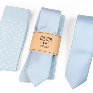 May include: A light blue patterned sock, a light blue tie with a brown label that reads "Trevor Best Man", and a light blue solid tie.