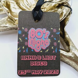 Può includere: Un'etichetta nera con un nastro bianco. L'etichetta presenta una grafica colorata degli anni '80 con il testo "Anna's Last Disco" e "25th May 2025".