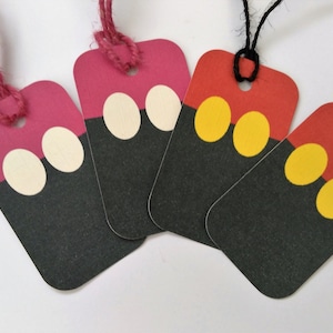 May include: Four gift tags with a Mickey Mouse design. The tags are red, pink, and yellow with black accents. Each tag has two white, yellow, or cream colored circles on the black portion of the tag.