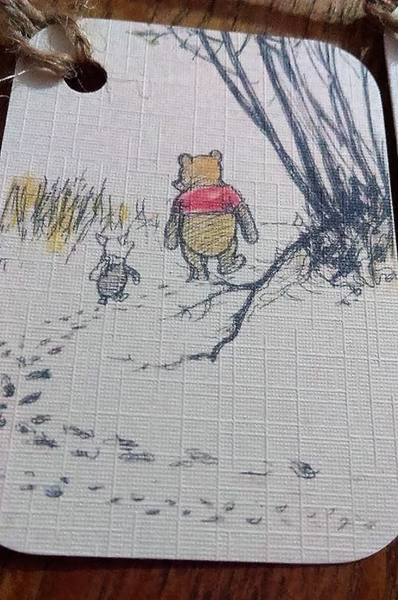 May include: A Winnie the Pooh and Piglet illustration on a white card with a brown background. The illustration shows Winnie the Pooh and Piglet walking away from the viewer. Winnie the Pooh is wearing a red shirt and Piglet is wearing a black shirt. The illustration is surrounded by a brown border.