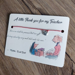 Könnte beinhalten: Eine weiße Karte mit einer roten Schnur und einem silbernen Anhänger, auf dem "Danke an meine Lehrerin" steht. Die Karte enthält ein Zitat aus Matilda von Roald Dahl: "Es besteht kein Zweifel, dass sie dieses seltene Talent besaß, von jedem kleinen Kind unter ihrer Obhut geliebt zu werden."