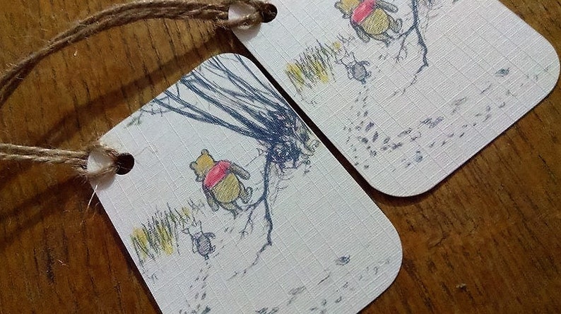 May include: Two Winnie the Pooh gift tags with a white background and brown twine. The tags feature a black and white illustration of Winnie the Pooh walking through the Hundred Acre Wood. The text on the tag reads "Pooh Bear".