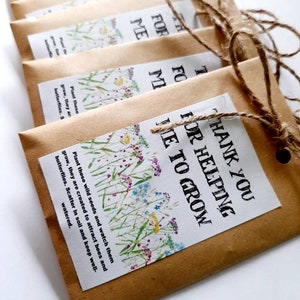 May include: Six brown paper envelopes with twine tied around them. Each envelope has a printed label with a floral design and the text "Thank you for helping me to grow". The envelopes contain wildflower seeds.