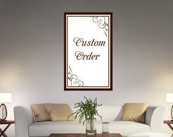 May include: A framed rectangular sign with the words "Custom Order" in brown script. The sign has a white background and a dark brown frame. Decorative brown flourishes are in the corners. The sign is hanging on a white wall.