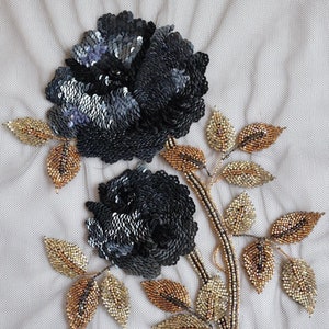 May include: A black and gold beaded floral applique with two roses and leaves. The roses are made of sequins and the leaves are made of small beads.