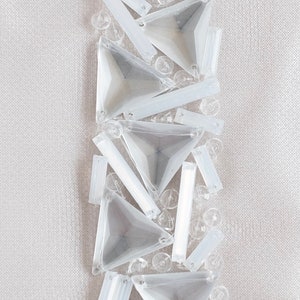 May include: A close-up of a white fabric with a vertical row of clear, iridescent, triangular and rectangular sequins.