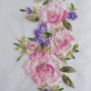 May include: Embroidered floral design with pink and white roses, purple flowers, and green leaves. The design is on a white fabric background.