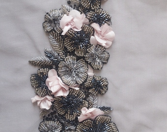 May include: A delicate floral design featuring pink fabric flowers and silver and black beads. The design is embroidered on a light gray fabric.