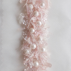 Könnte beinhalten: Nahaufnahme einer rosa-weißen Perlenborte mit Perlenakzenten. Die Borte besteht aus zartem Stoff und Perlen und ist perfekt, um jedem Projekt einen Hauch von Eleganz zu verleihen.