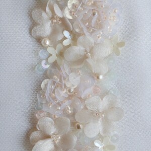 May include: A delicate white lace trim with pearl-like beads and sequins. The trim features a floral design with small, delicate flowers.