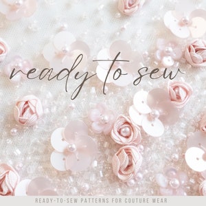 May include: Close-up of a white fabric with pink fabric flowers and white sequins. The text "ready to sew" is written in cursive on the fabric.
